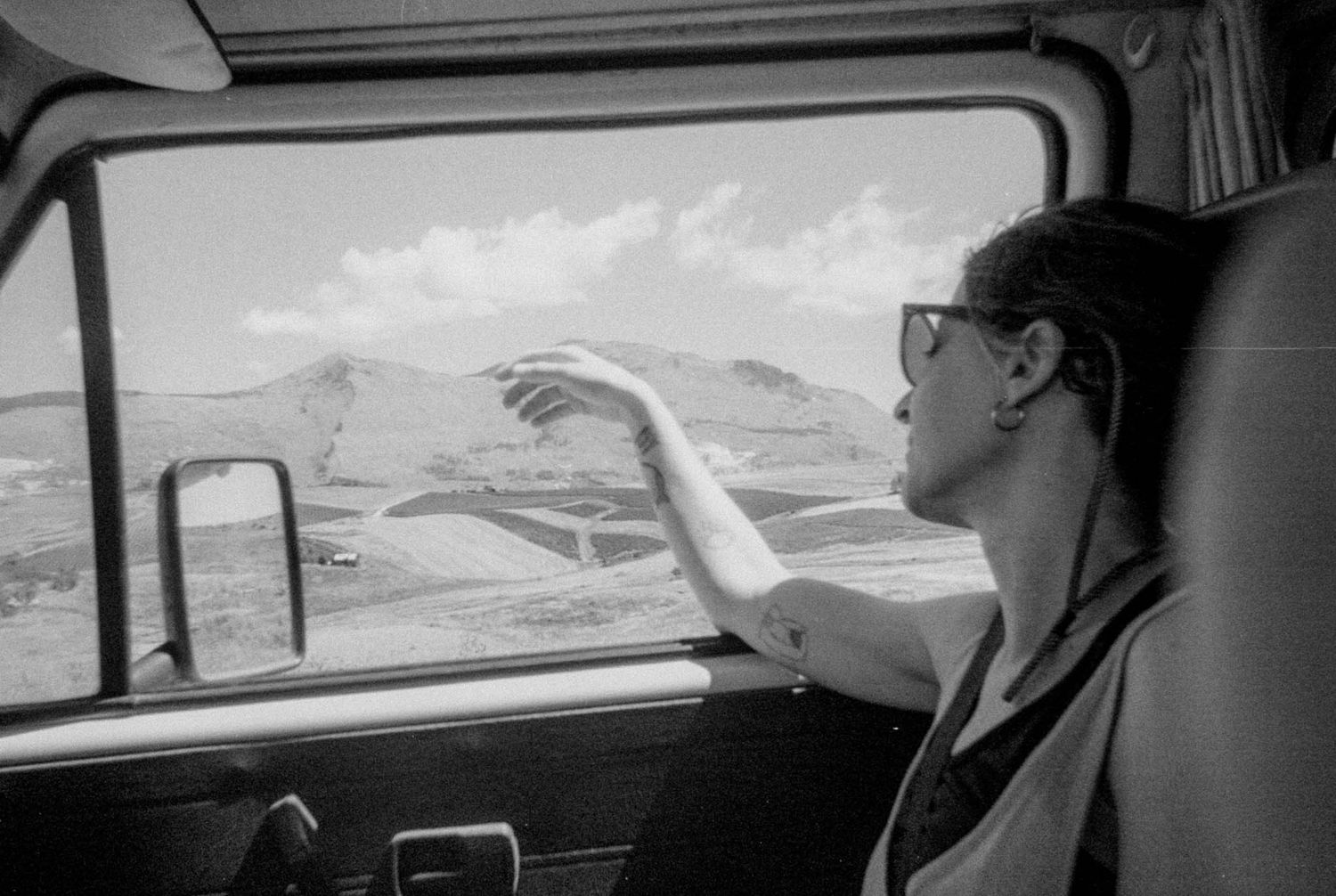 Black and white photo of passengers inside a car looking out windows during a road trip.
