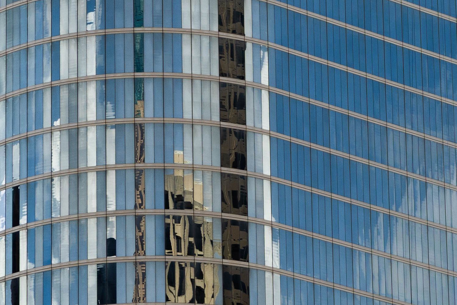 Modern glass office building facade with blue reflective windows and geometric patterns in sunlight.