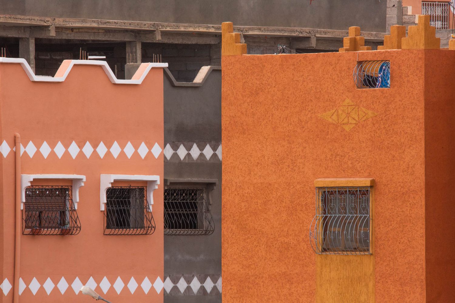 A row of terracotta orange buildings with decorative white trim and wrought iron balconies along a street.