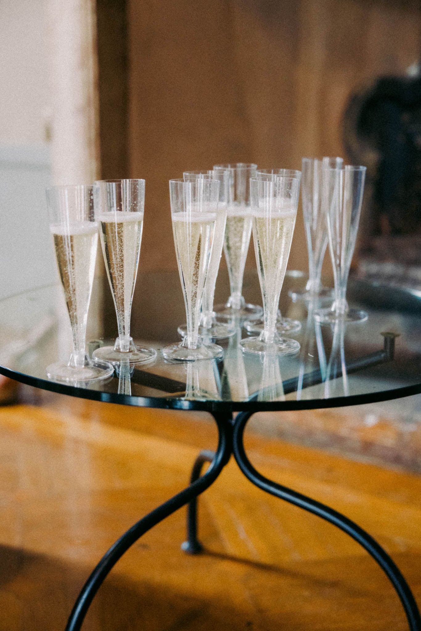 Champagne flutes filled with sparkling wine arranged on a round glass table with black metal base.