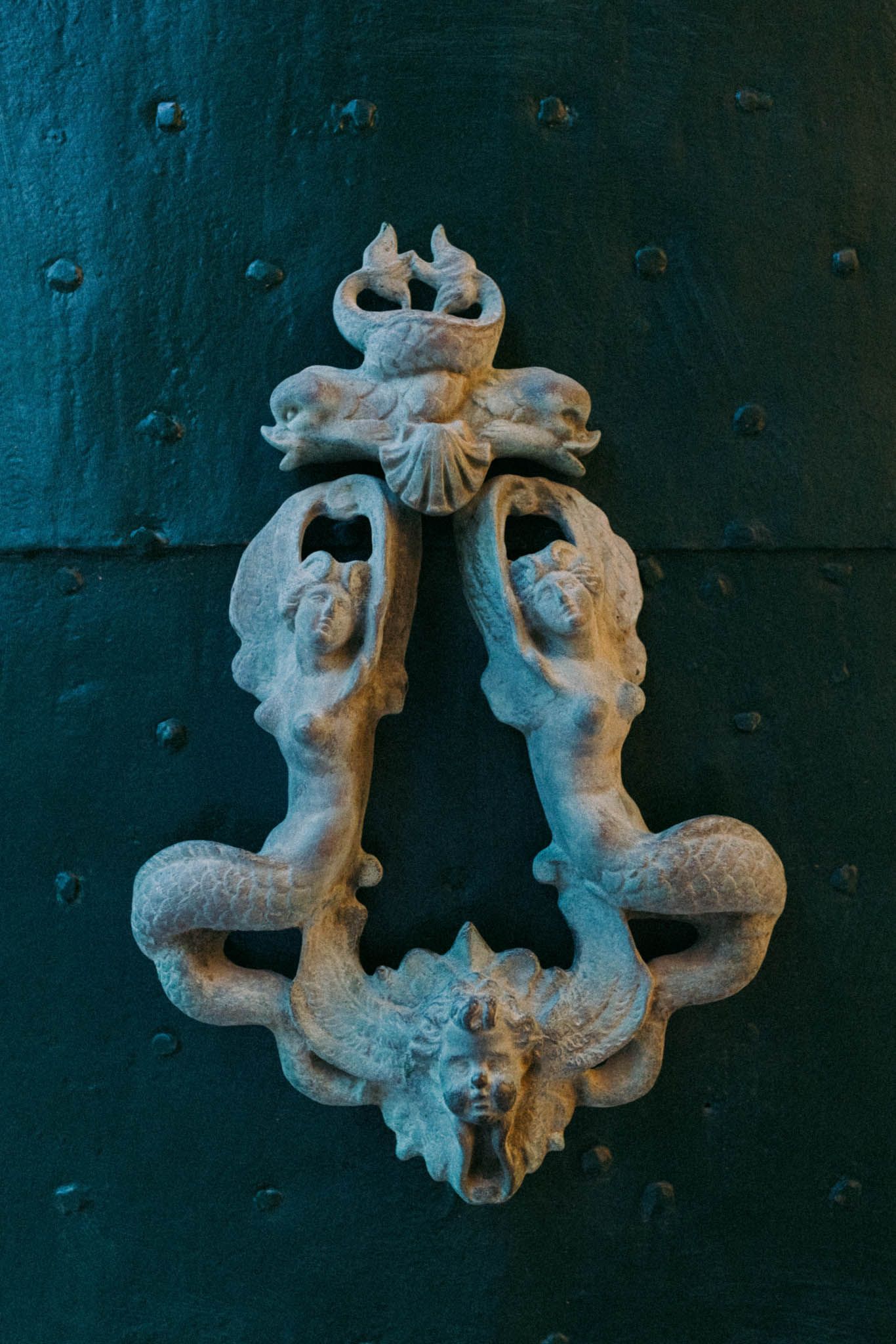 Decorative mermaid sculptures holding a cross mounted on a dark teal wall in a series of artistic detail shots.