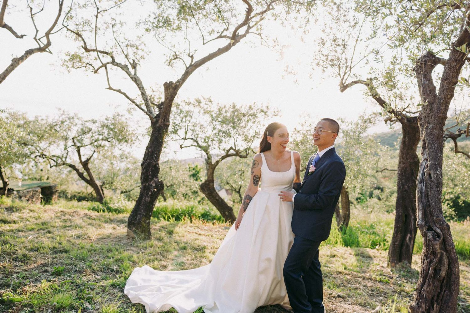 A couple shares a romantic moment in a sunlit olive grove during their wedding photoshoot.