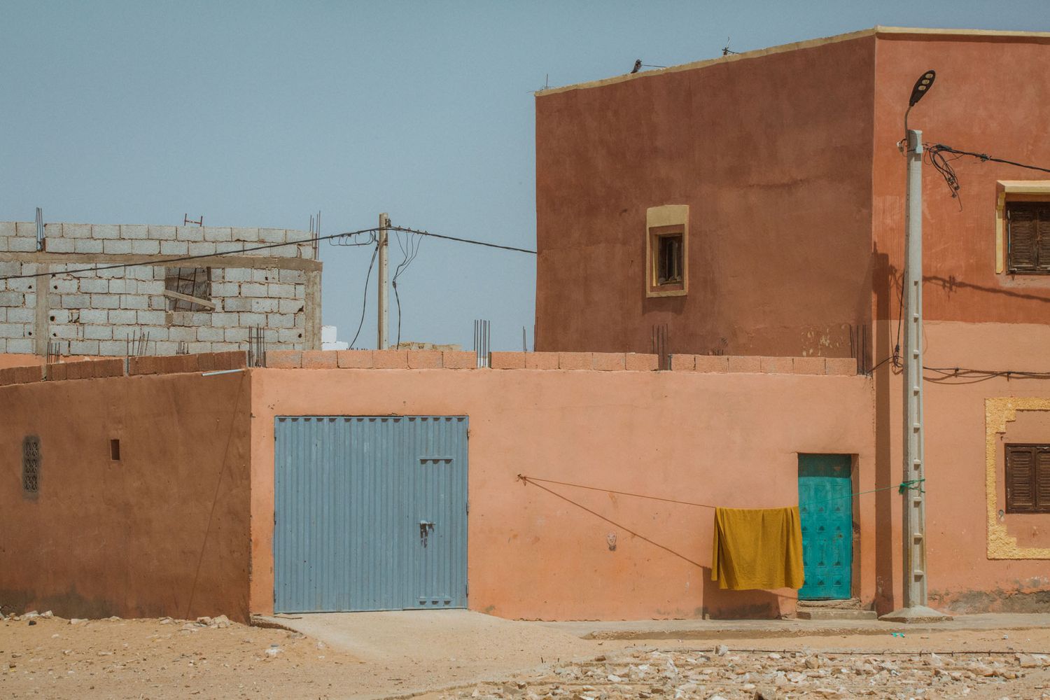 Desert buildings with blue and green doors against terracotta colored walls under a cloudy sky.