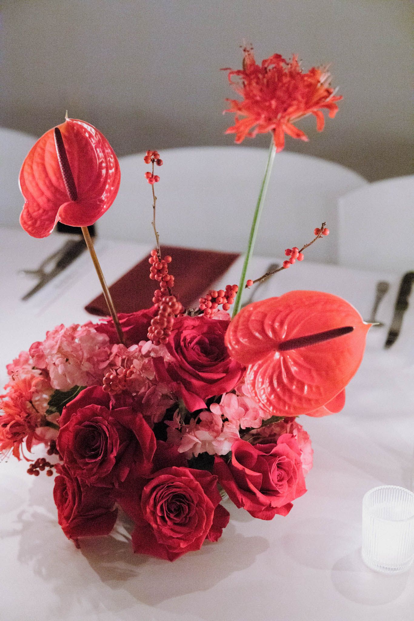 A vibrant floral arrangement featuring red roses, anthurium flowers, and berries displayed in a modern setting.