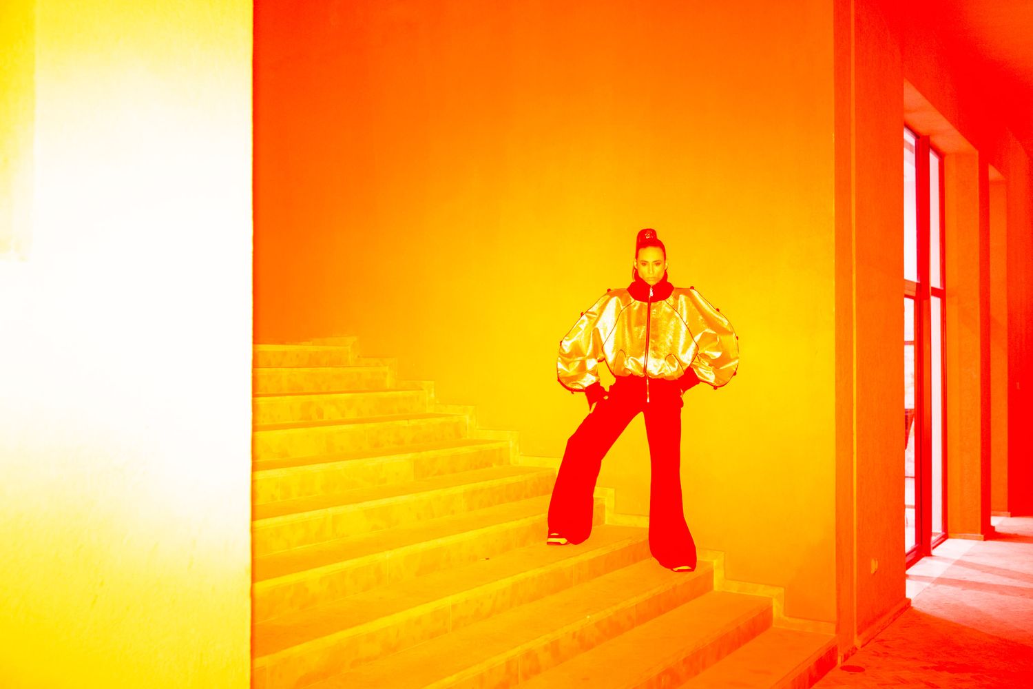 Figure in retro-style bell bottom pants stands in vibrant orange and yellow hallway with dramatic lighting.