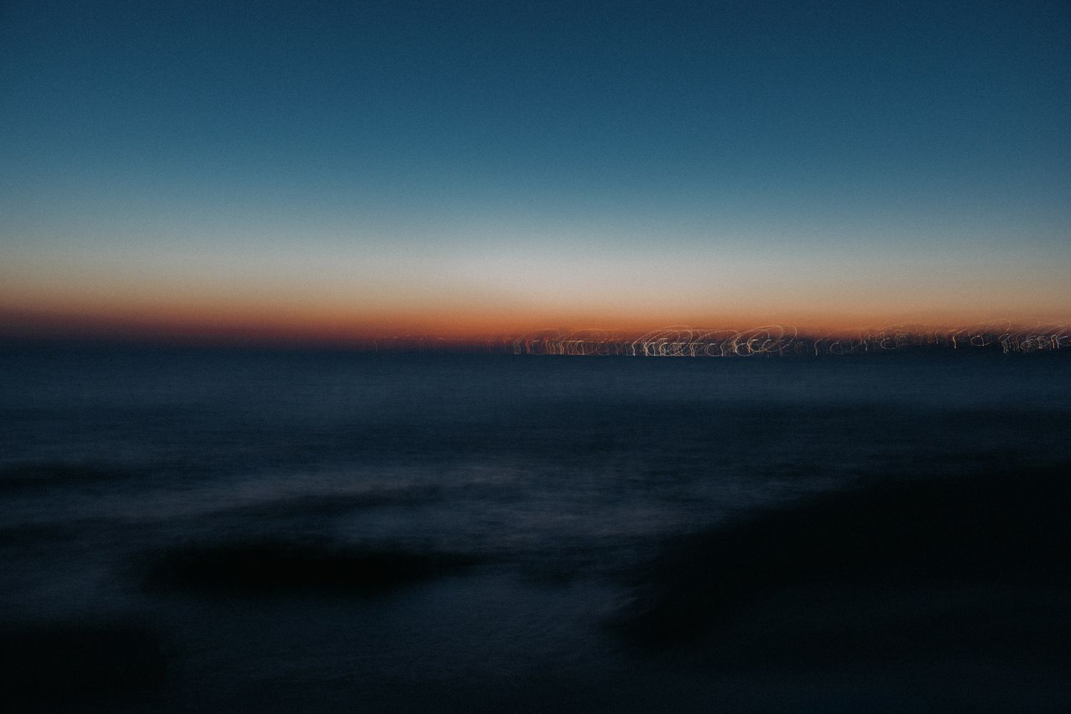 A panoramic sequence of sunset photos showing the sky transitioning from bright orange to deep blue over the horizon.