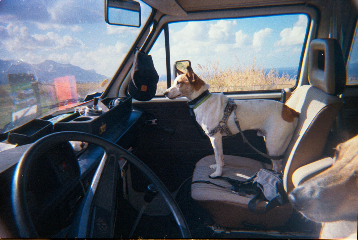View through a car windshield while driving on a road with mountains and blue skies in the background.