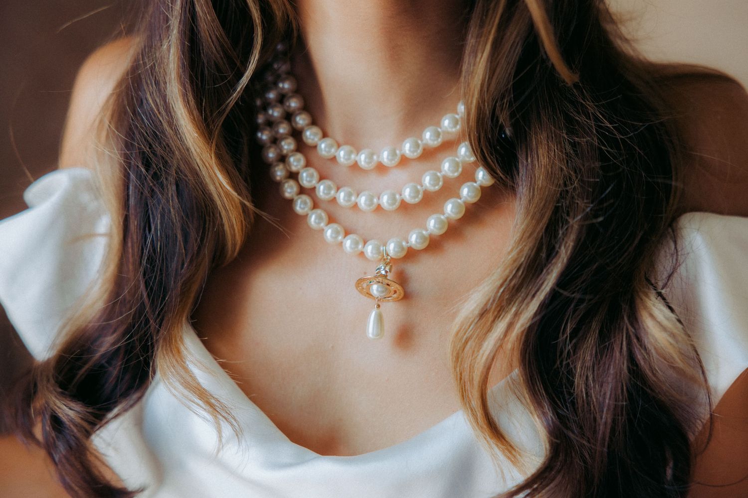 A double-strand pearl necklace with a pendant charm adorns a neckline against a white blouse.