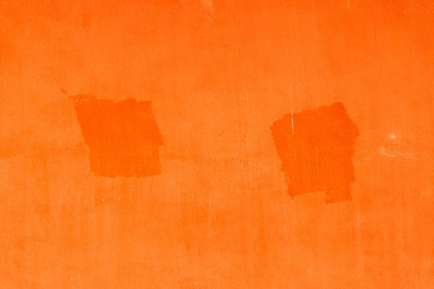 Orange painted wall with two rectangular patches showing previous paint color beneath.