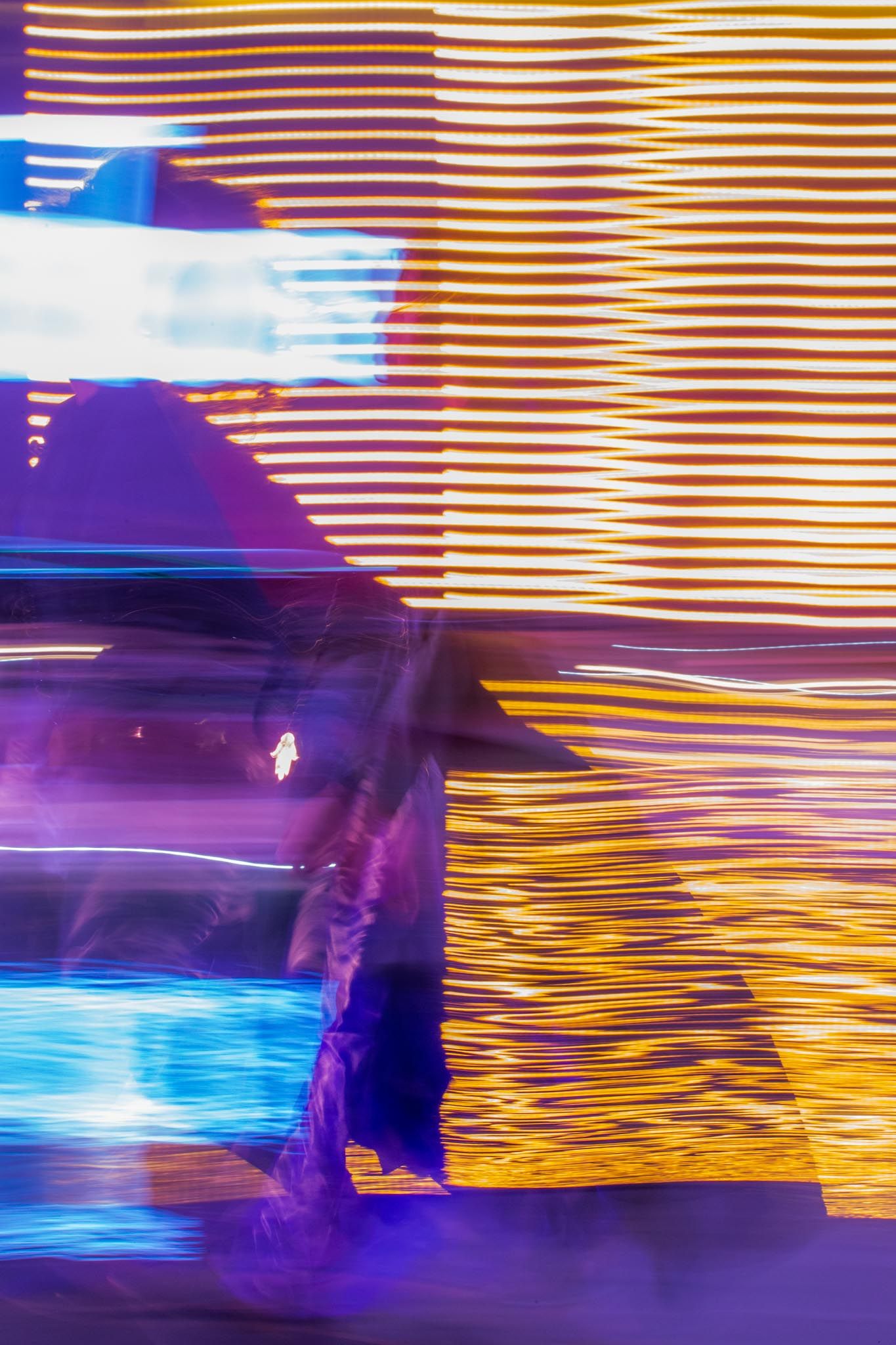 Abstract light painting with streaks of purple, blue and orange creating a dynamic motion blur effect against a dark background.
