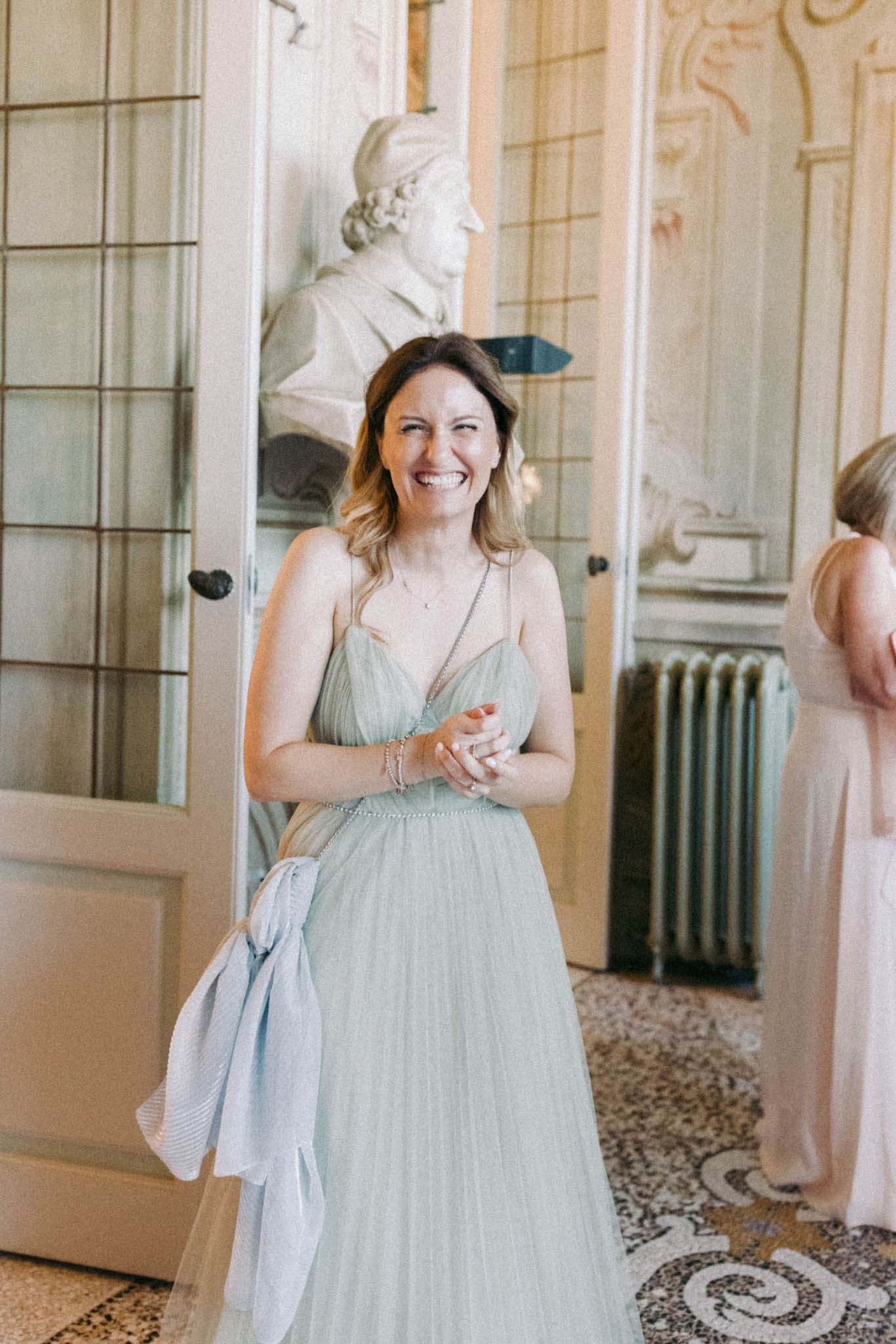 A person in a light mint green tulle gown twirls in an elegant room with white walls and decorative moldings.