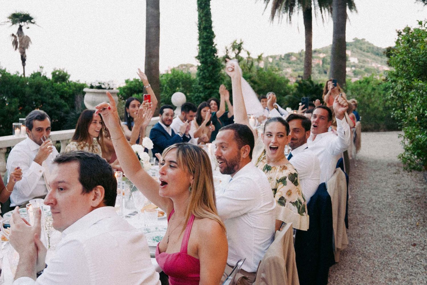 Wedding guests dancing and celebrating together with raised arms at an outdoor reception party.