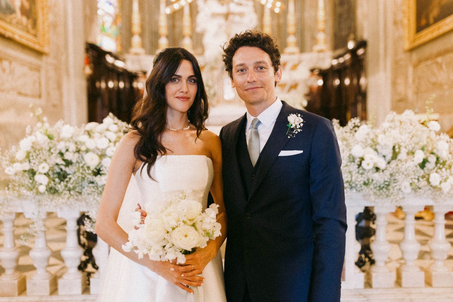 A couple shares intimate moments in a luxurious wedding venue decorated with elegant white floral arrangements.