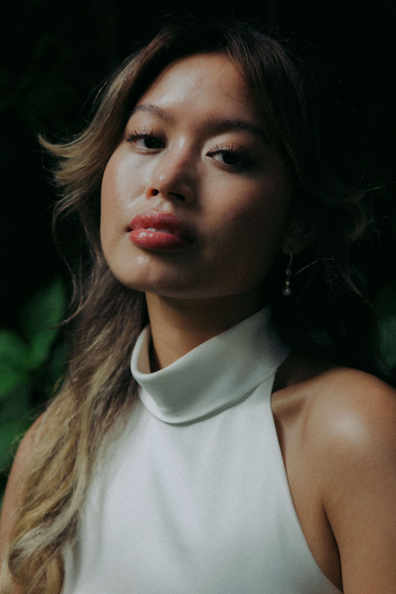 A woman in a white halter top poses expressively against a dark background in a series of artistic portraits.