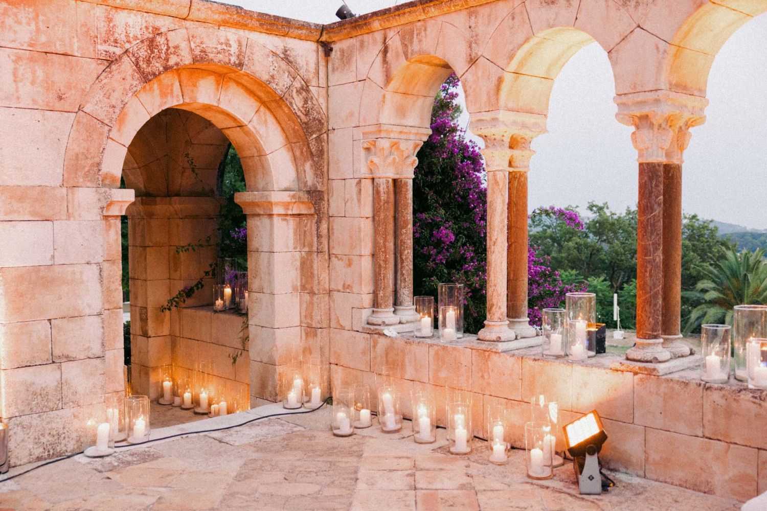 Pink stone arched colonnade with ornate architectural details and purple flowering vines at a historic building.