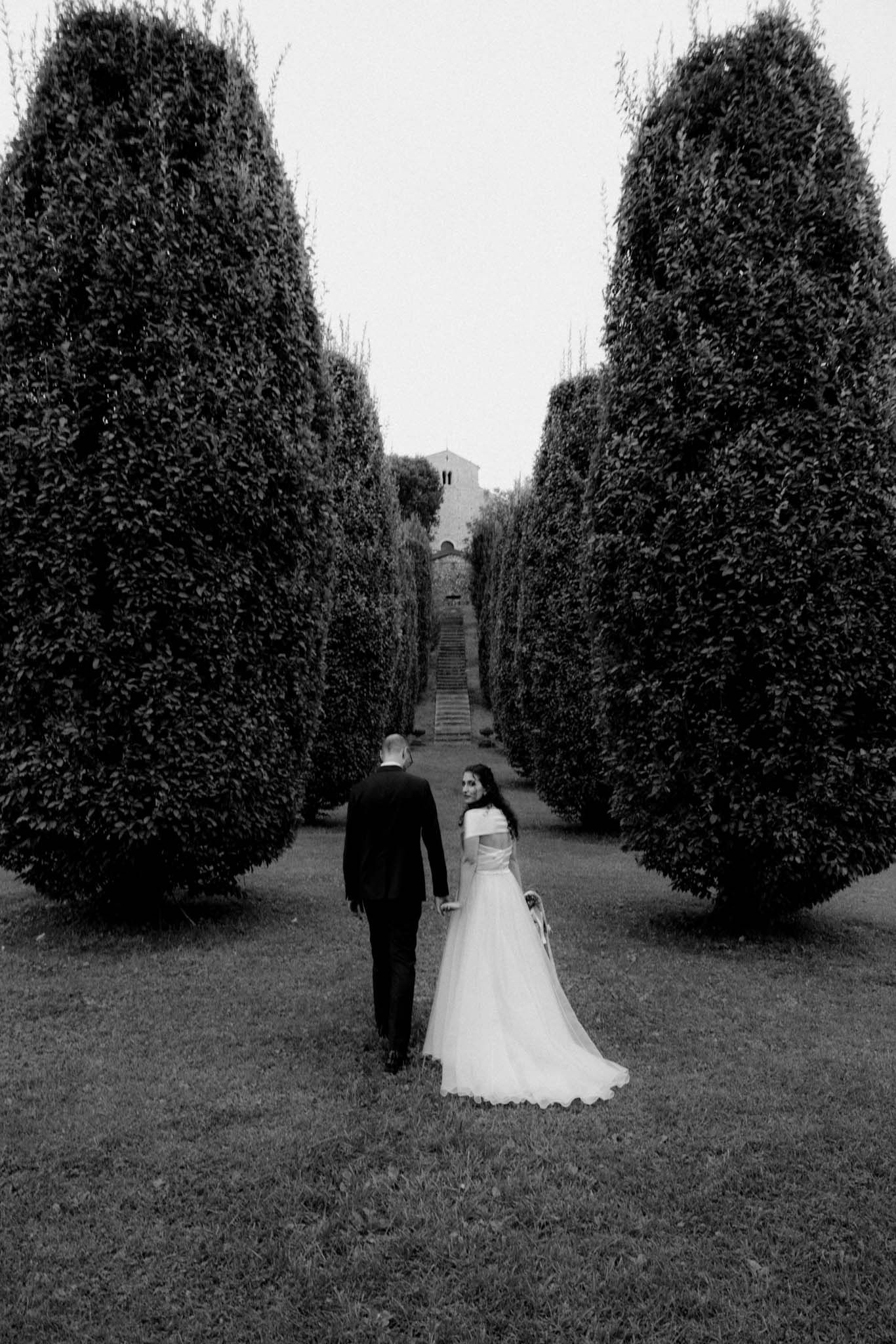 Black and white wedding photos among tall manicured hedges in a formal garden setting.