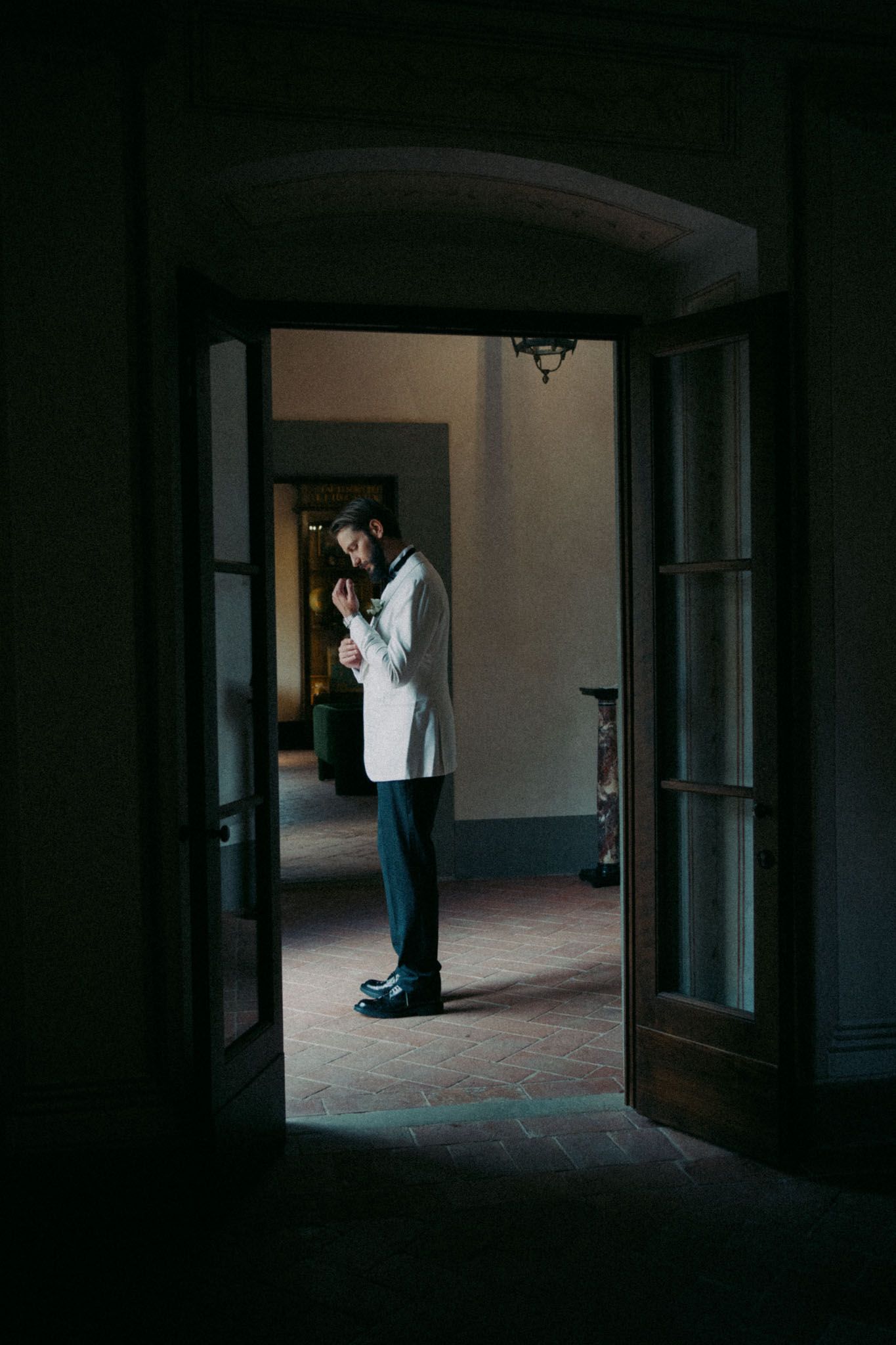 Silhouette of a person in formal attire standing in a dimly lit doorway of an elegant building.