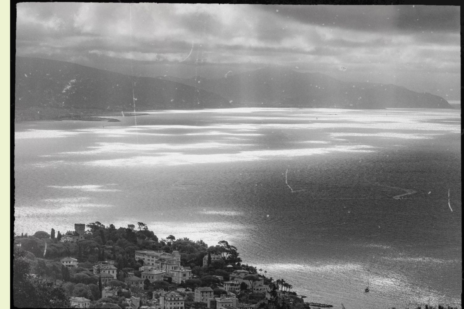 Panoramic black and white cityscape showing historic buildings and mountains against a dramatic cloudy sky.