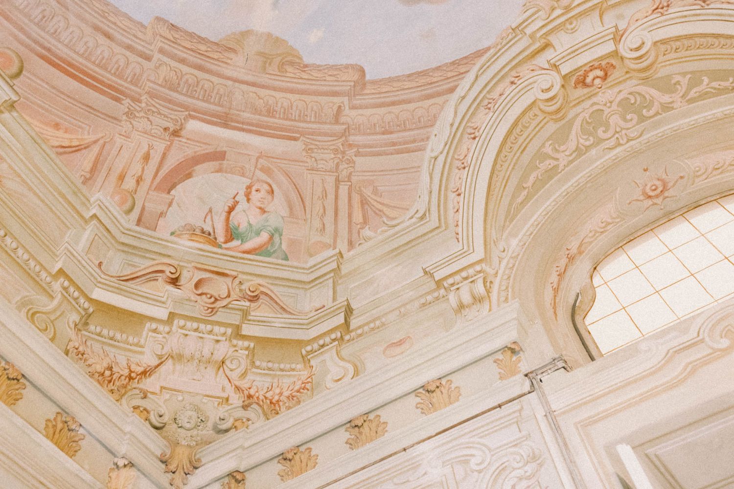 Ornate baroque ceiling with intricate white and gold decorative plasterwork and fresco paintings in a historic palace interior.