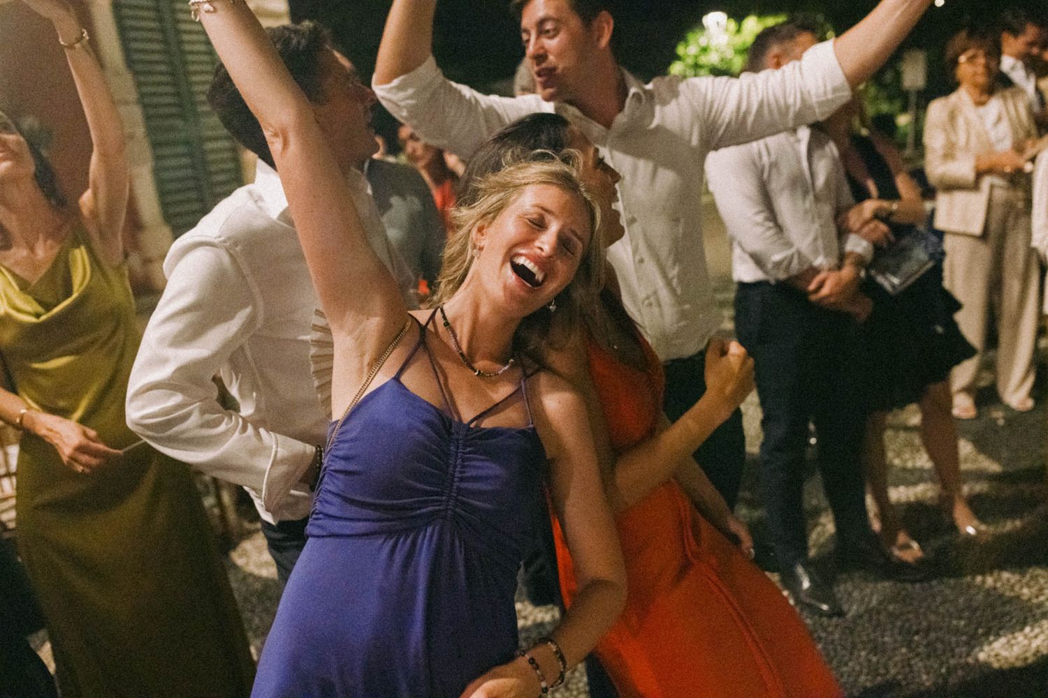 Wedding guests dance and celebrate joyfully on a crowded dance floor at an evening reception.