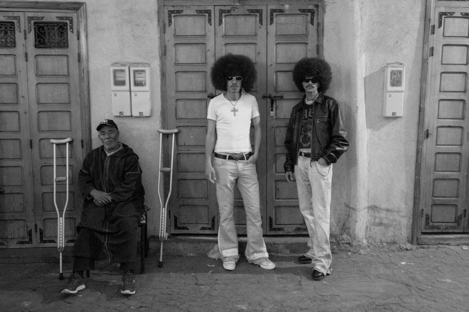 A series of black and white photographs showing people standing against walls and doorways in an urban setting.