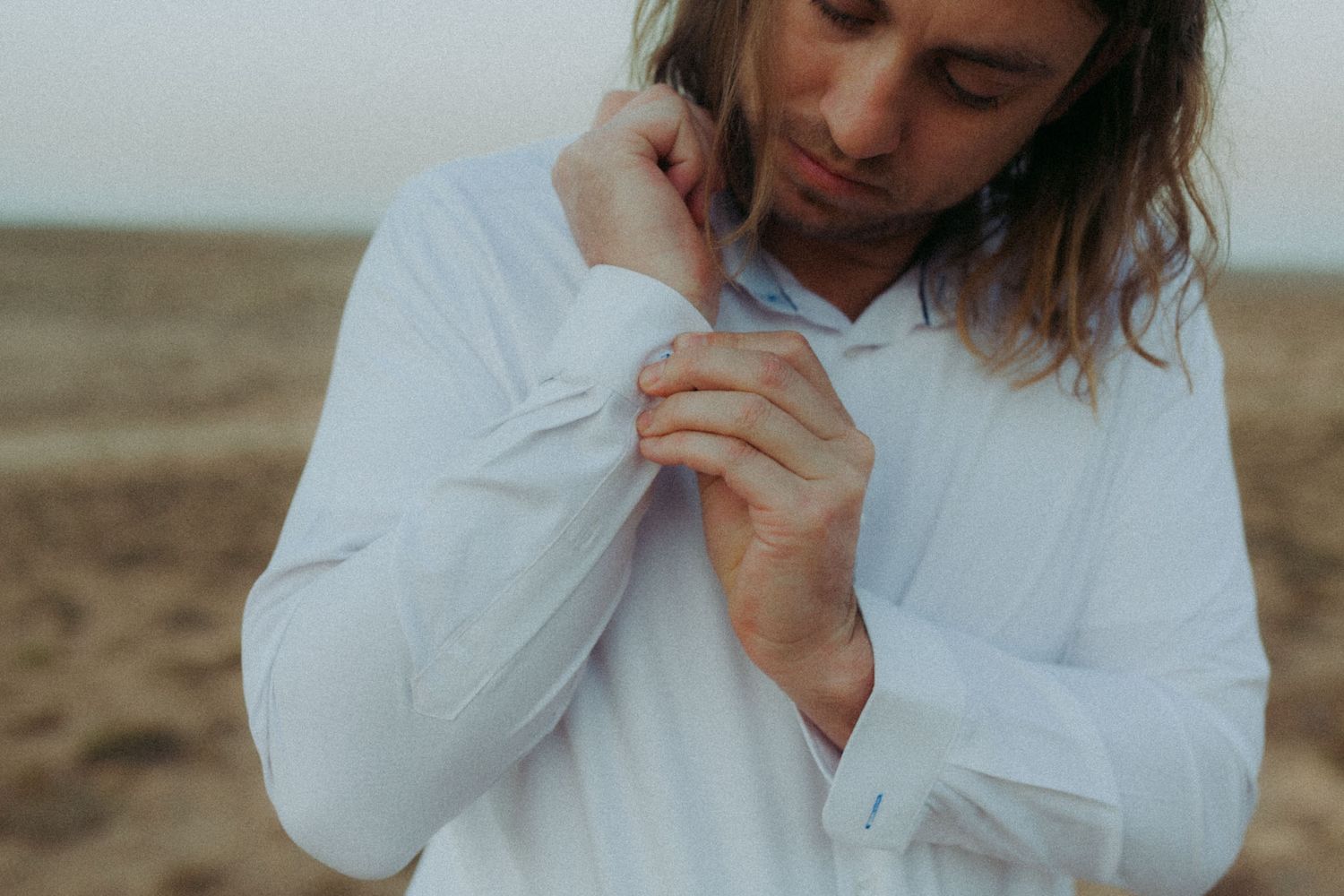 Person wearing white button-down shirt poses thoughtfully against natural outdoor setting.