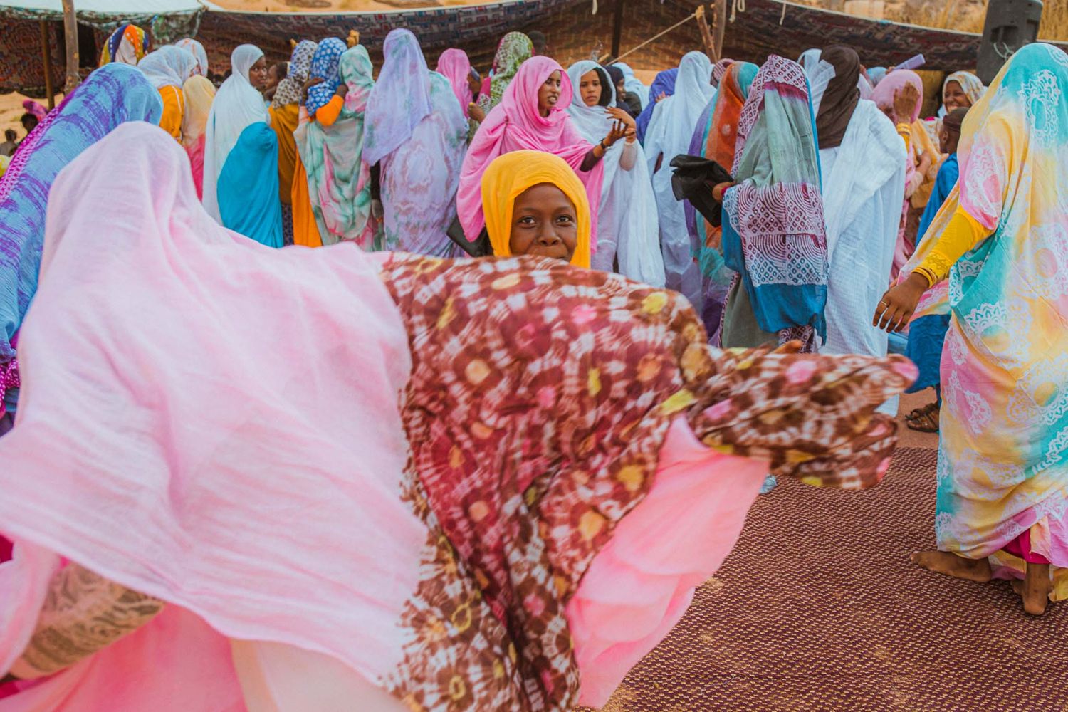 A group of people wearing colorful traditional clothing and headscarves gathered at an outdoor celebration.