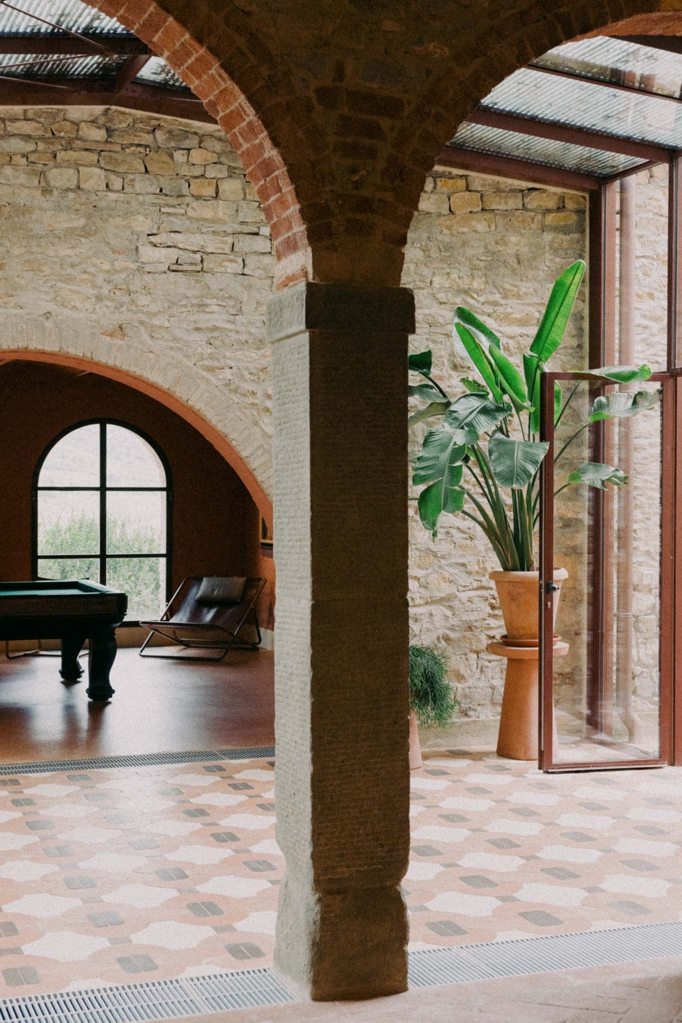 Interior stone archway corridor with brick columns, tiled floor, and potted plants in a Mediterranean-style building.