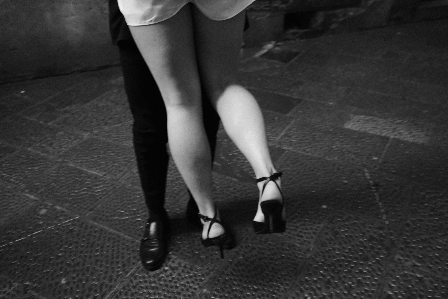Black and white close-up of feet in vintage dance shoes on a dark wooden floor.