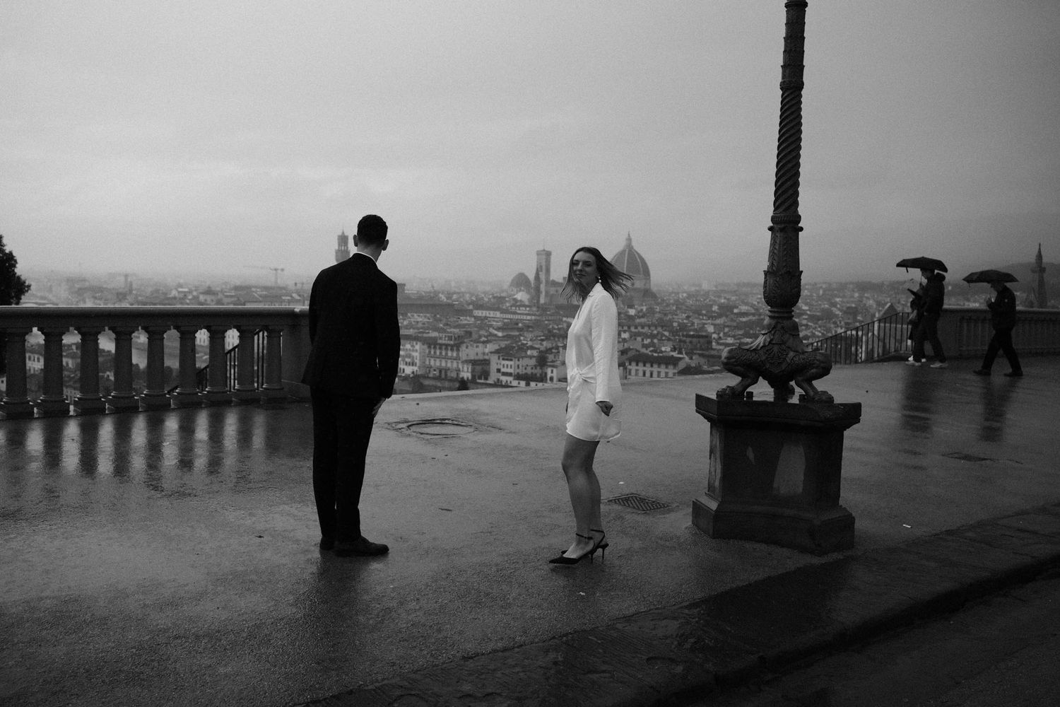 A black and white panoramic photo shows people silhouetted against a misty cityscape from an elevated viewpoint.