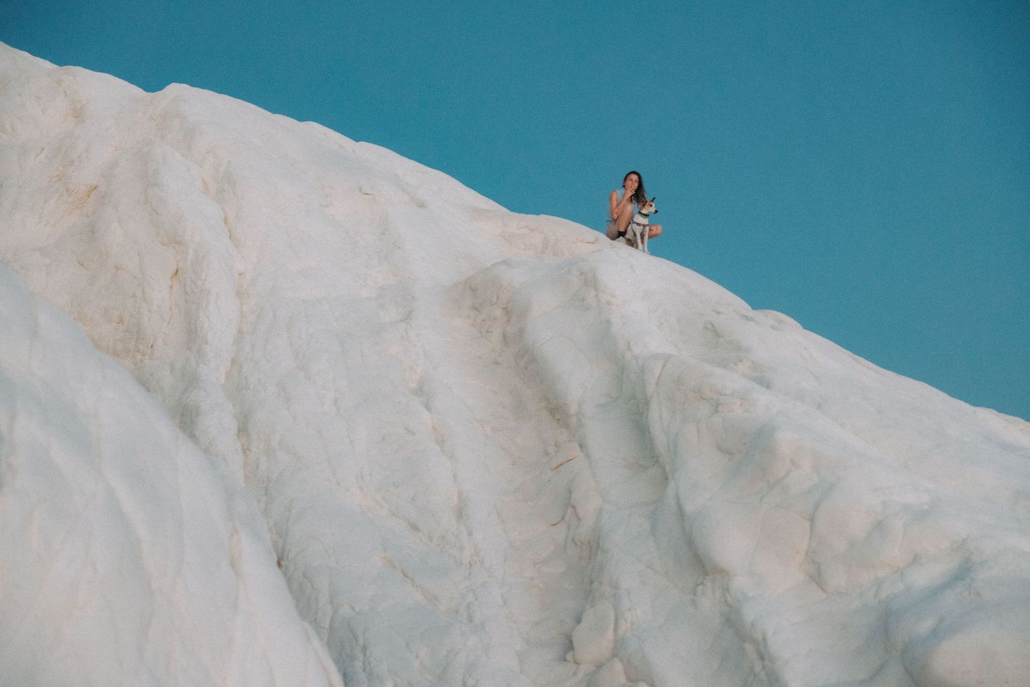 A skier carves down a steep snowy slope against a bright blue sky backdrop.
