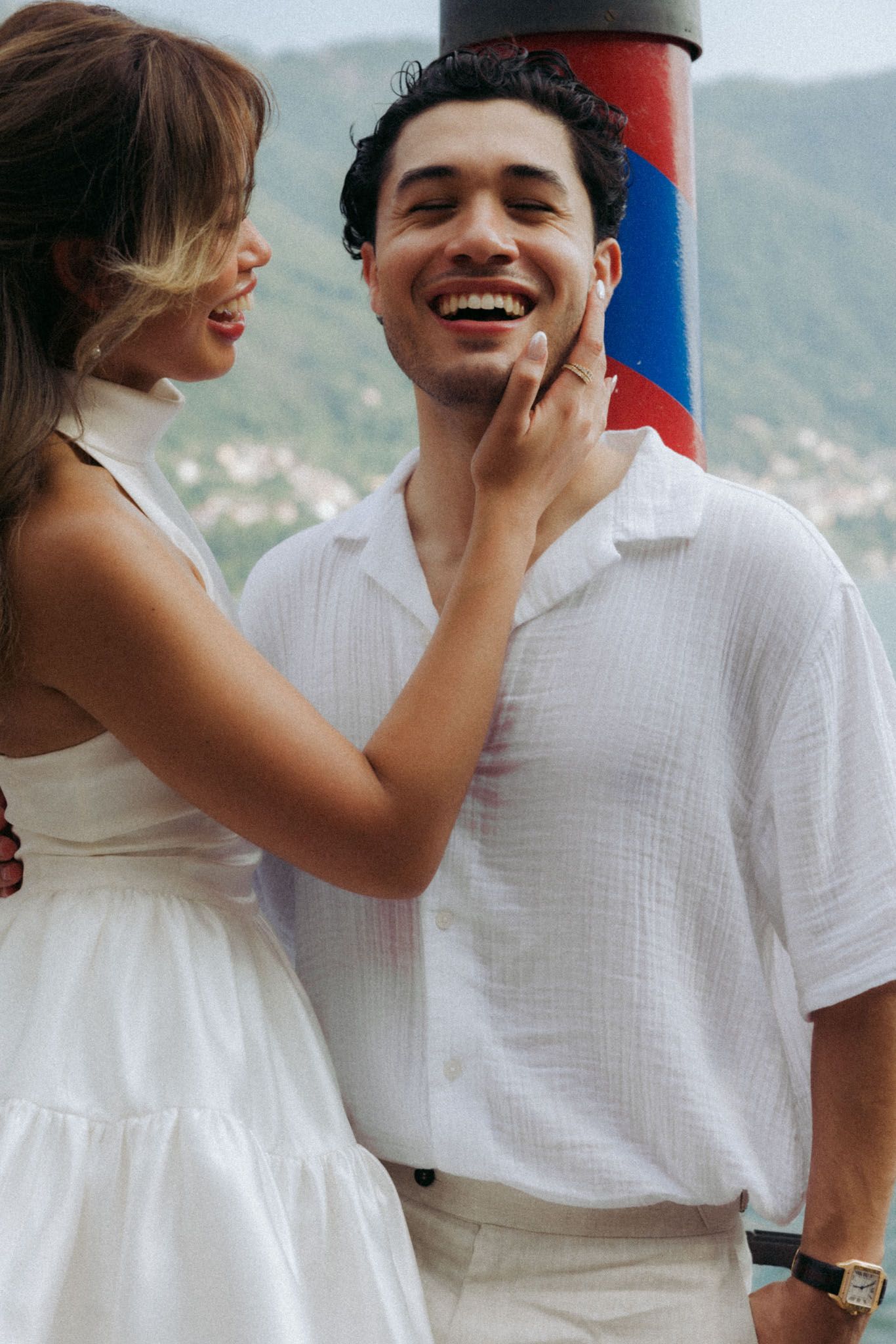 A playful couple in white outfits share intimate moments against a mountainous backdrop.
