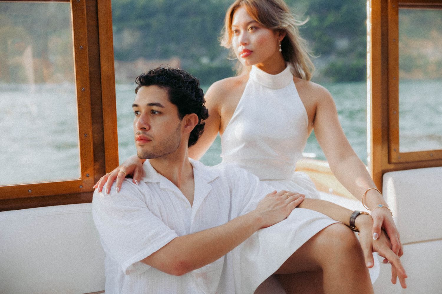 A couple in white outfits poses romantically on a boat deck during a sunny day on the water.