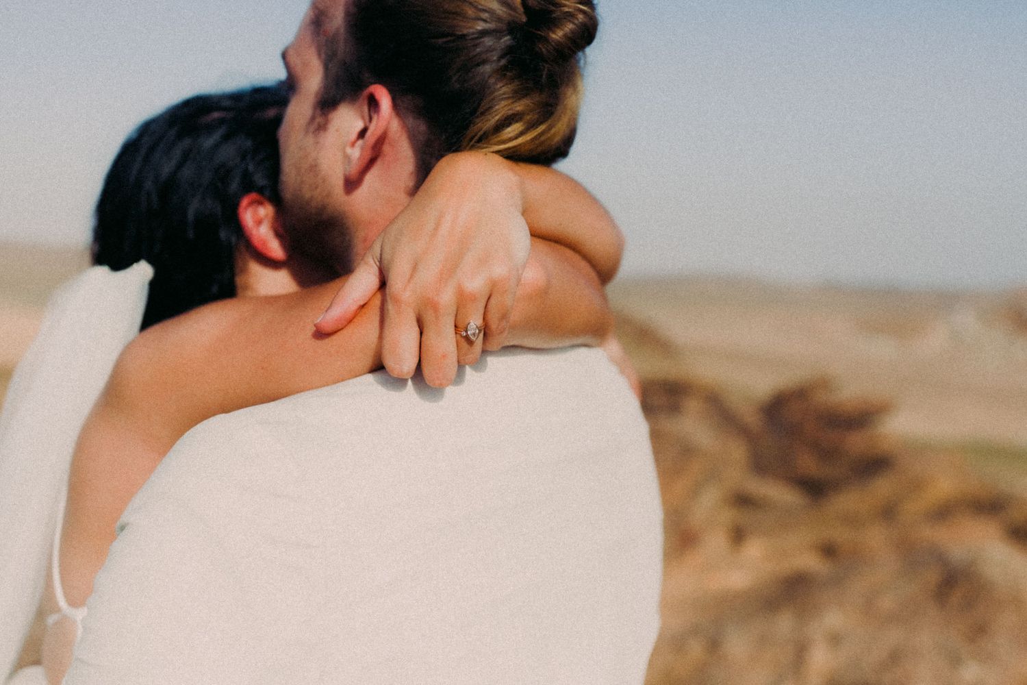 Romantic couple embraces in a desert landscape with warm sunlight and mountains in the background.