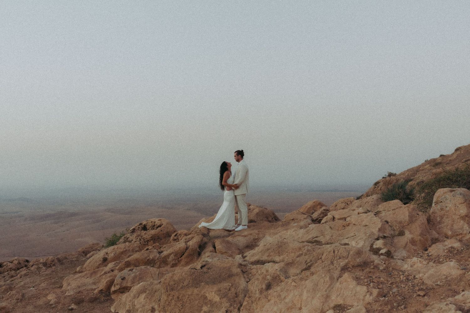 Hikers stand atop rugged desert cliffs overlooking vast canyon landscapes at sunset.