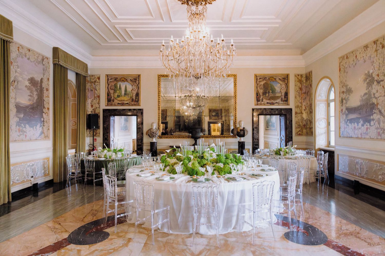 Elegant white and gold ballroom with crystal chandeliers and round tables set for a formal dining event.
