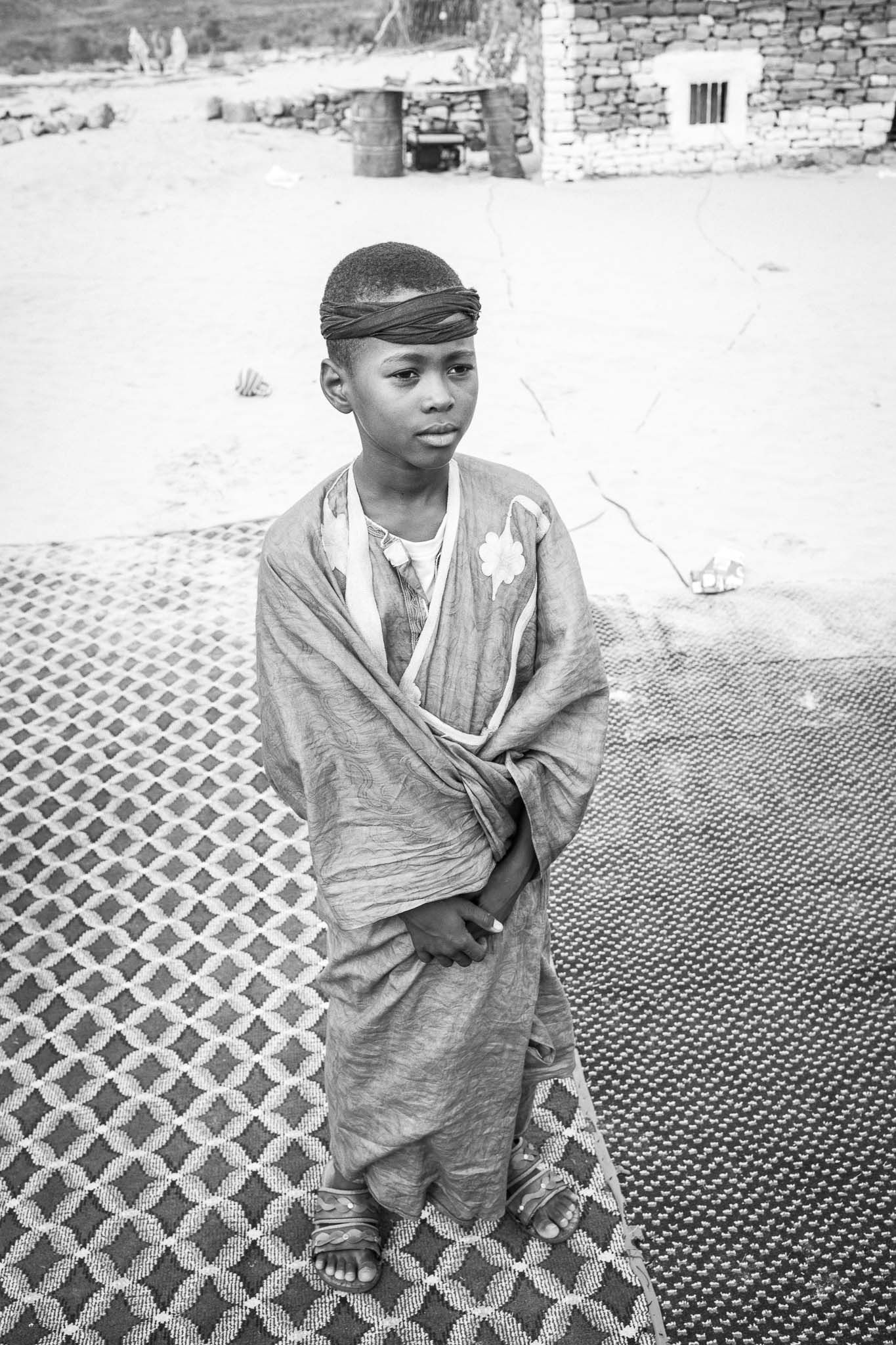 A series of black and white photographs showing a child in traditional African clothing standing on a patterned surface.
