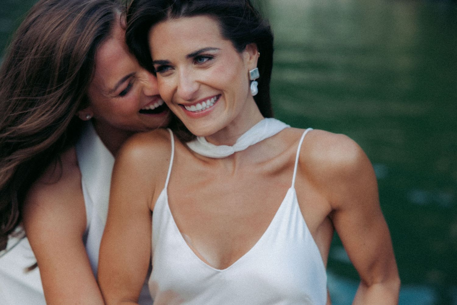 A group of bridesmaids in white dresses share a candid laughing moment together outdoors.