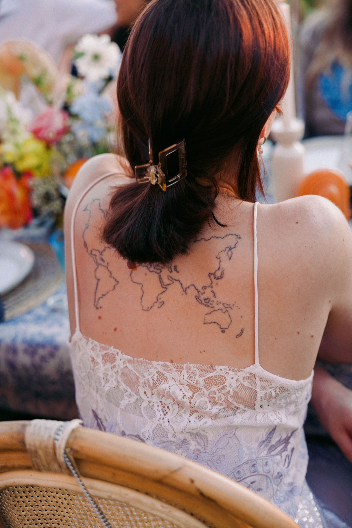 Back view of a delicate white lace wedding dress with a world map tattoo design visible on the wearer's shoulders.