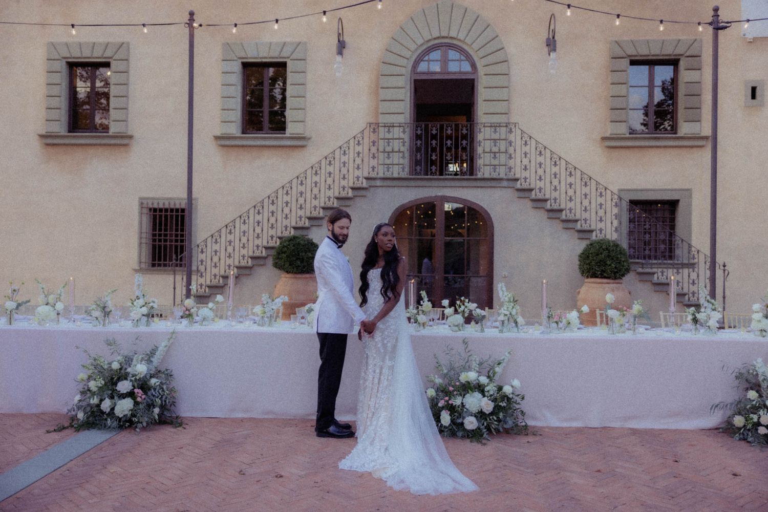 A bride and groom stand together at a rustic Italian villa courtyard during their wedding ceremony.