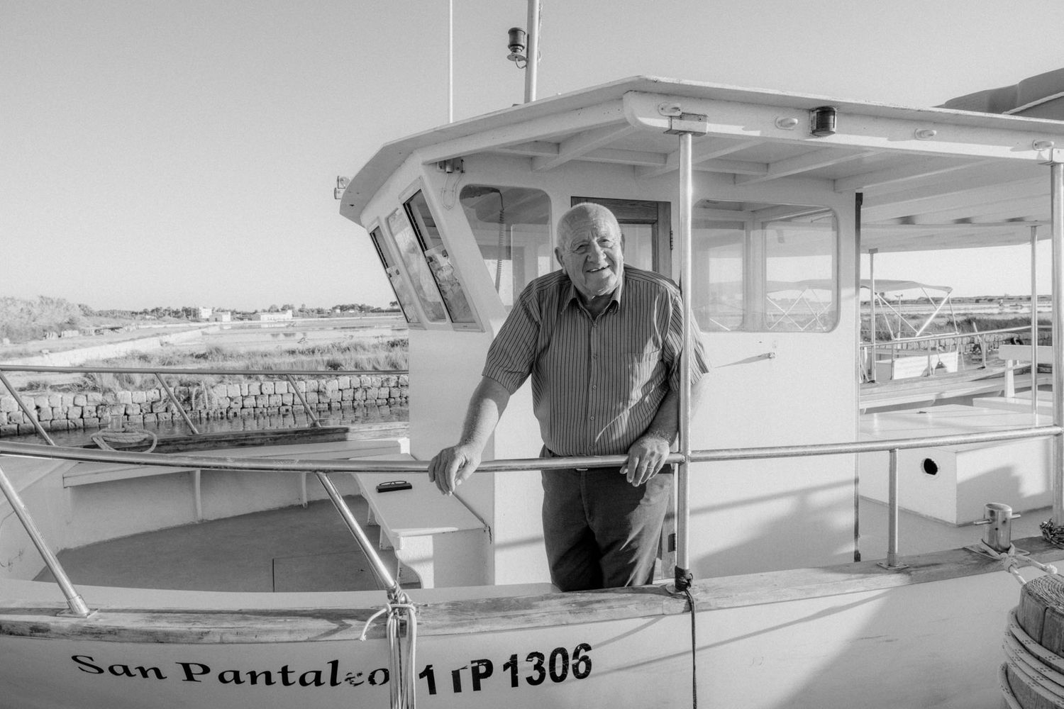 Black and white image of a person standing on a boat named San Pantaleo at a marina.