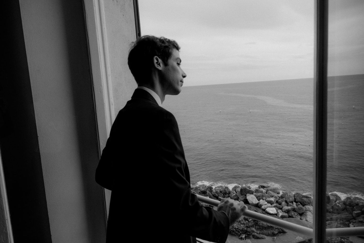 A person stands silhouetted in front of a window overlooking a coastal landscape and ocean view.