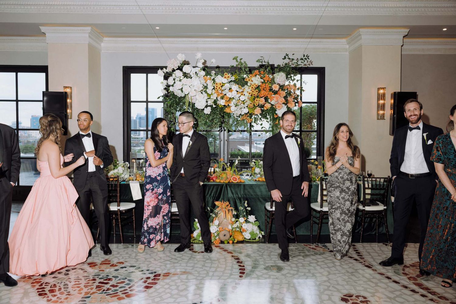 Wedding guests celebrate and dance together at an elegant reception venue decorated with floral arrangements.