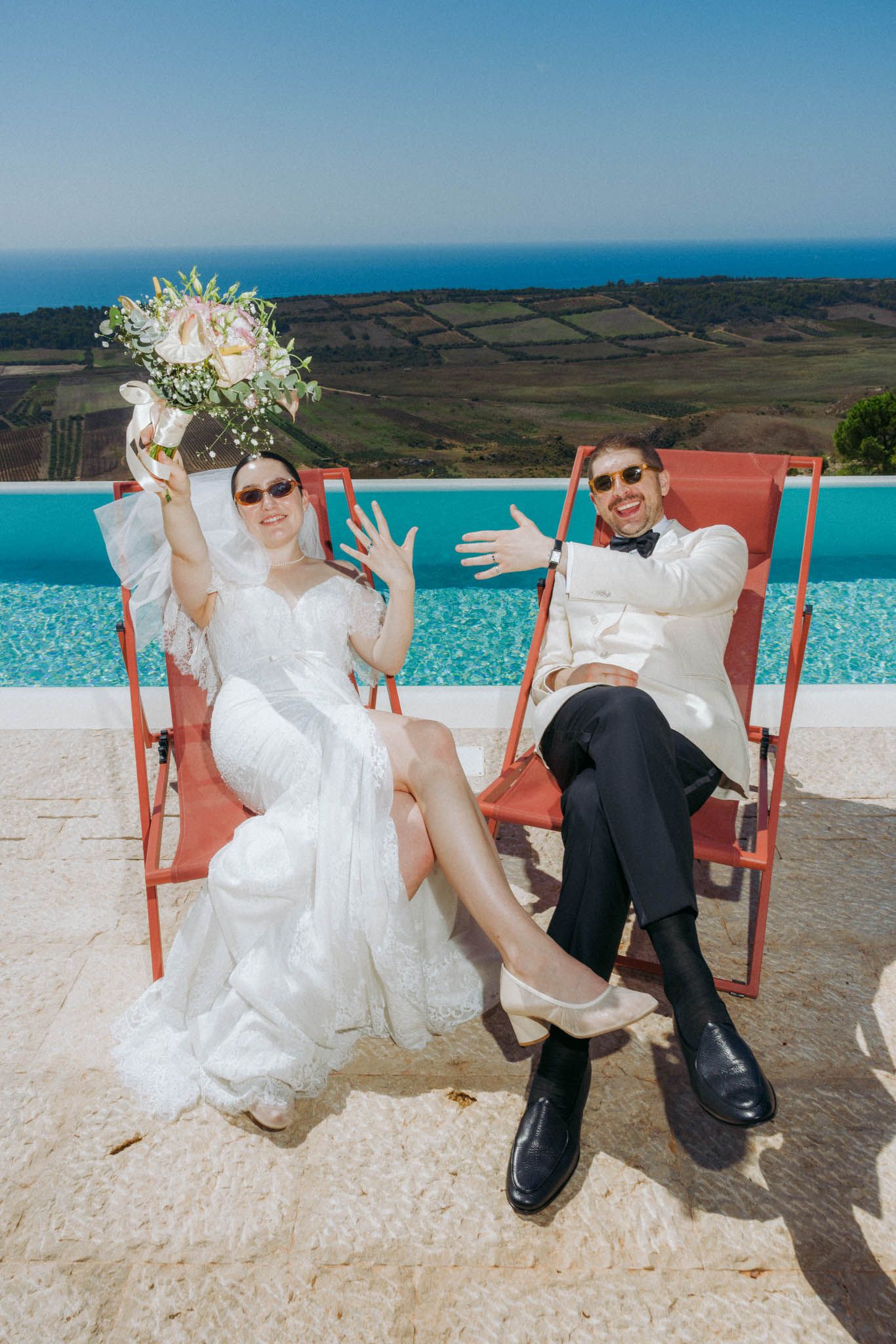 Newlywed couple poses playfully in sequence on orange deck chairs against scenic coastal backdrop.
