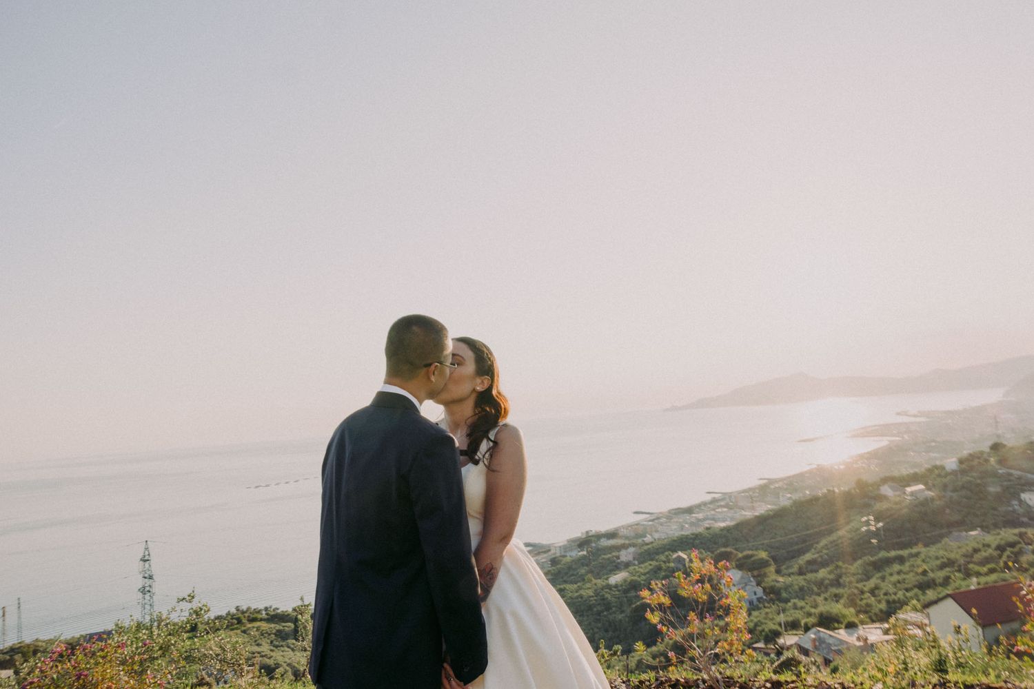 A couple shares an intimate moment on a hilltop overlooking a scenic coastal landscape at sunset.