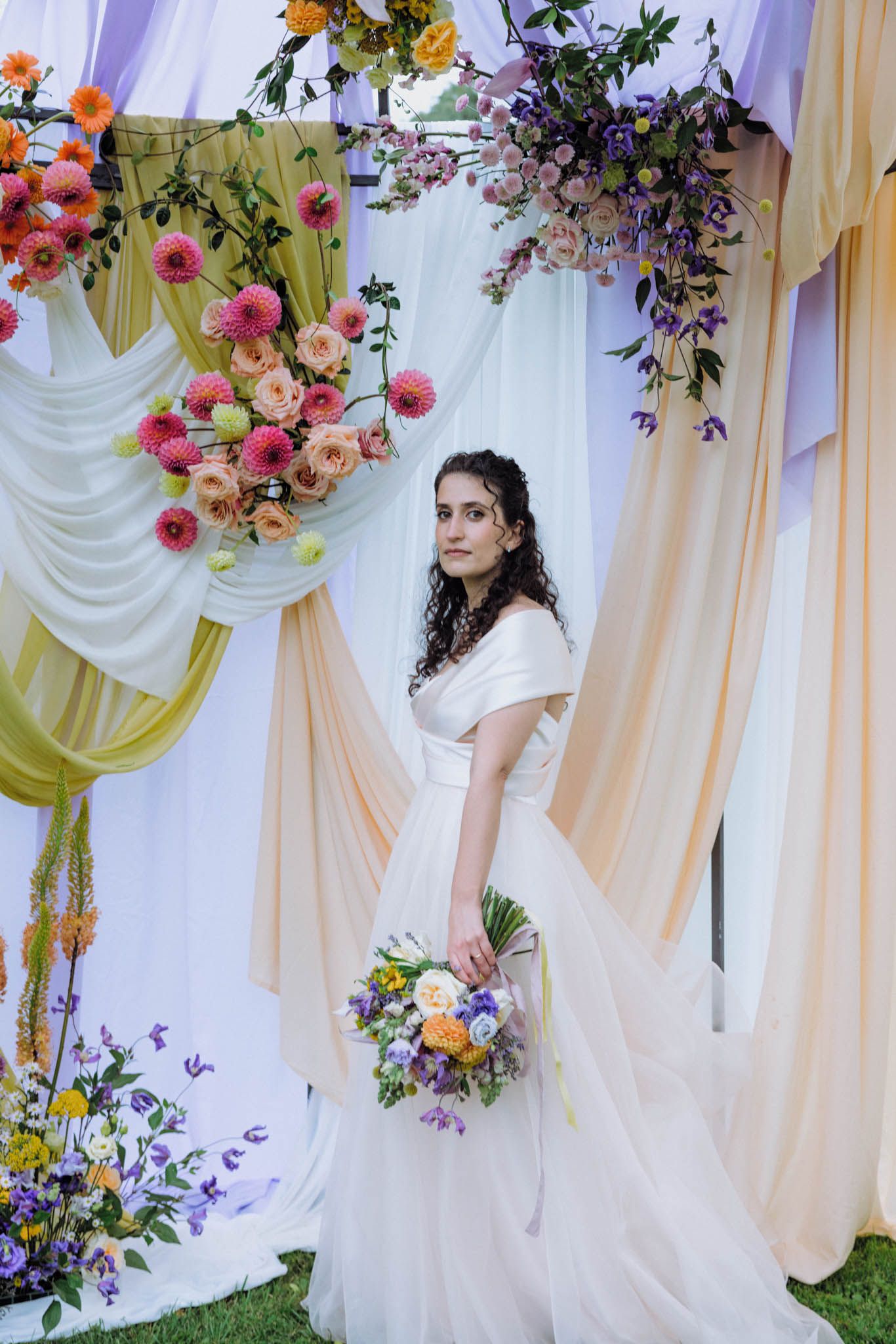 Elegant wedding backdrop with draped white fabric and colorful floral arrangements featuring orange and purple blooms.
