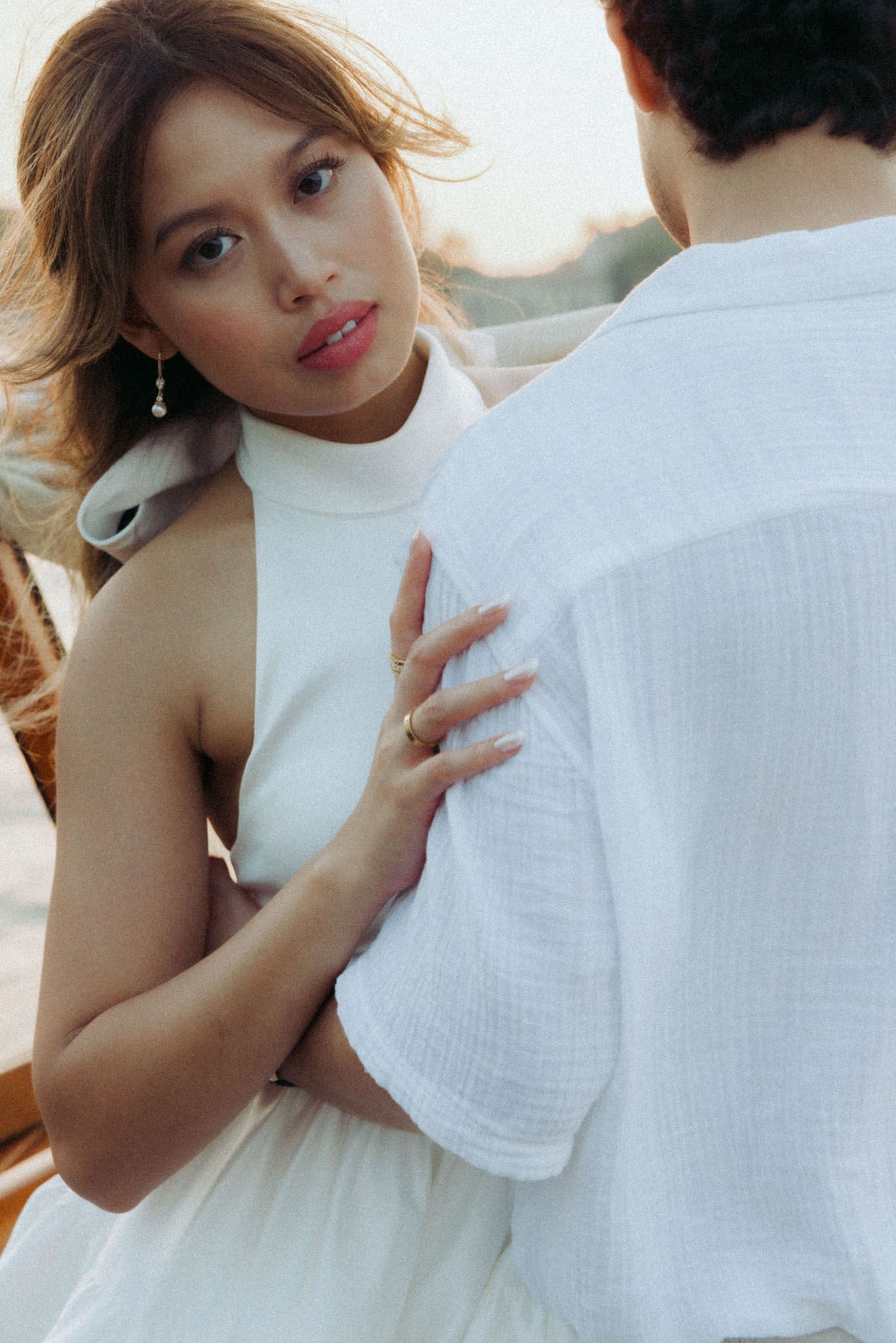 A person in a white dress embraces someone wearing a white shirt in a romantic pose.