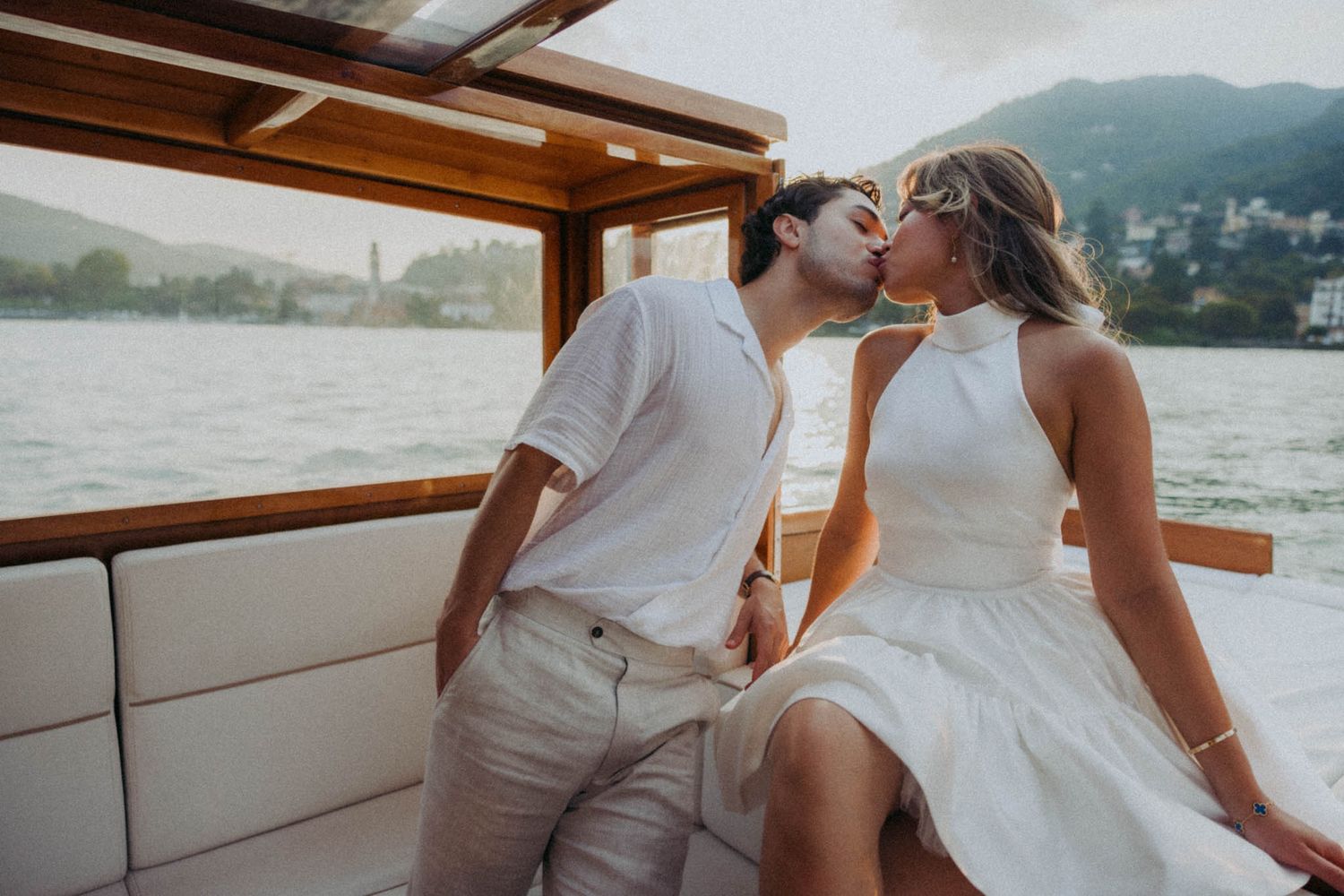 Couple in white attire sharing intimate moments aboard a boat during a romantic lake excursion.