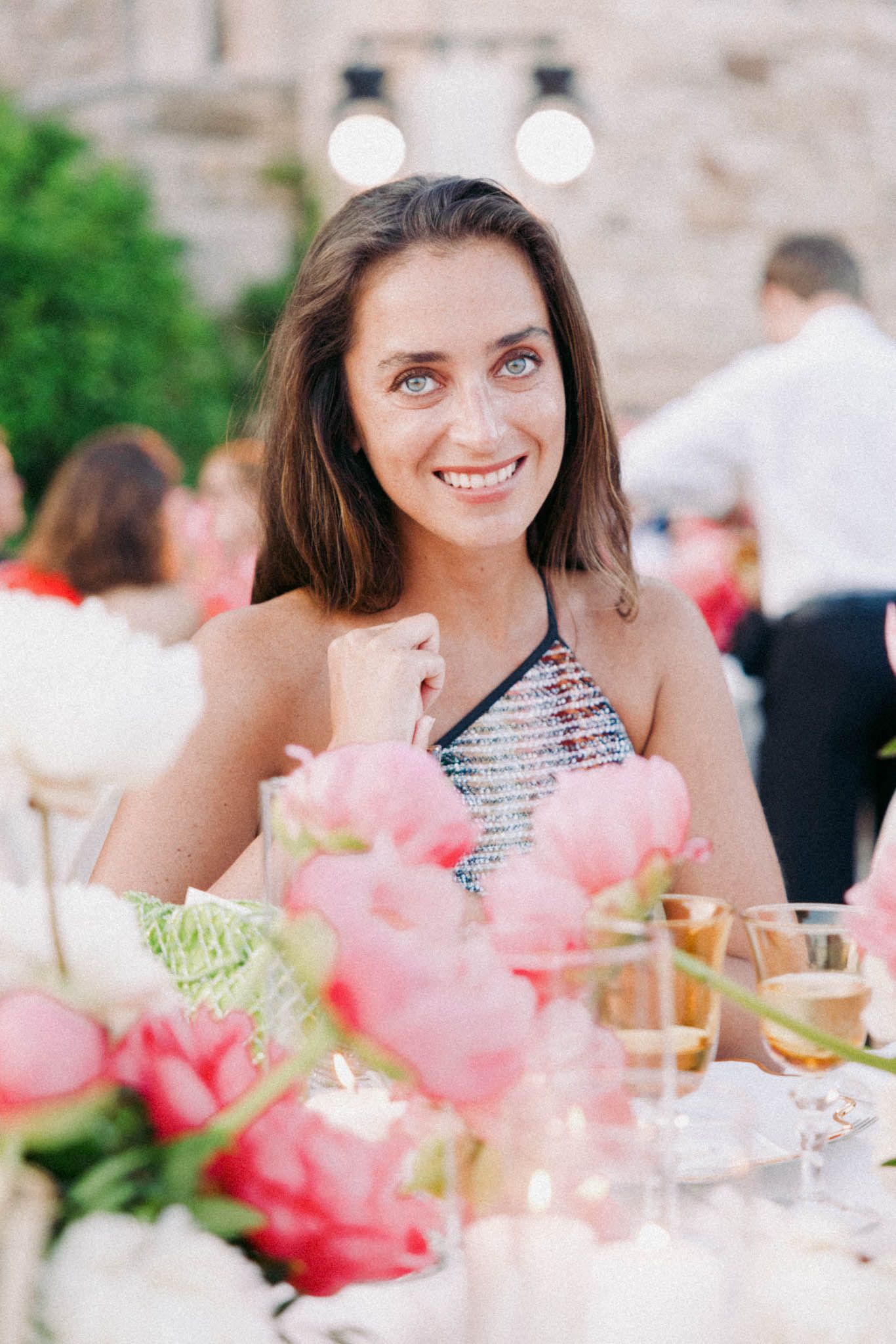 Elegant table setting at outdoor reception with pink peonies and glassware in warm evening light.