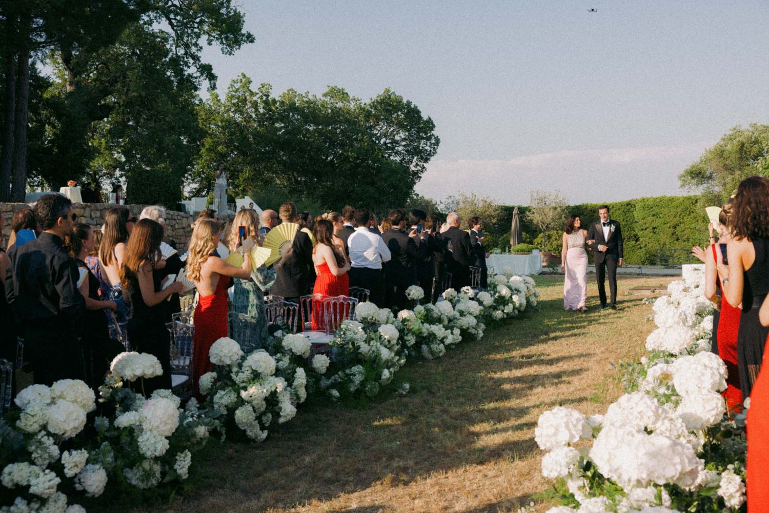 White floral arrangements line a garden path at an elegant outdoor wedding venue.